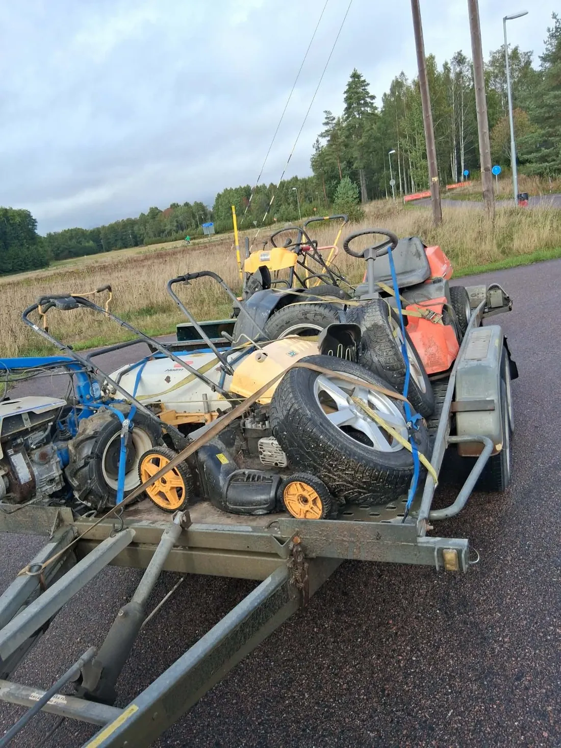 Släpvagn lastad med flera olika gräsklippare och mindre maskiner