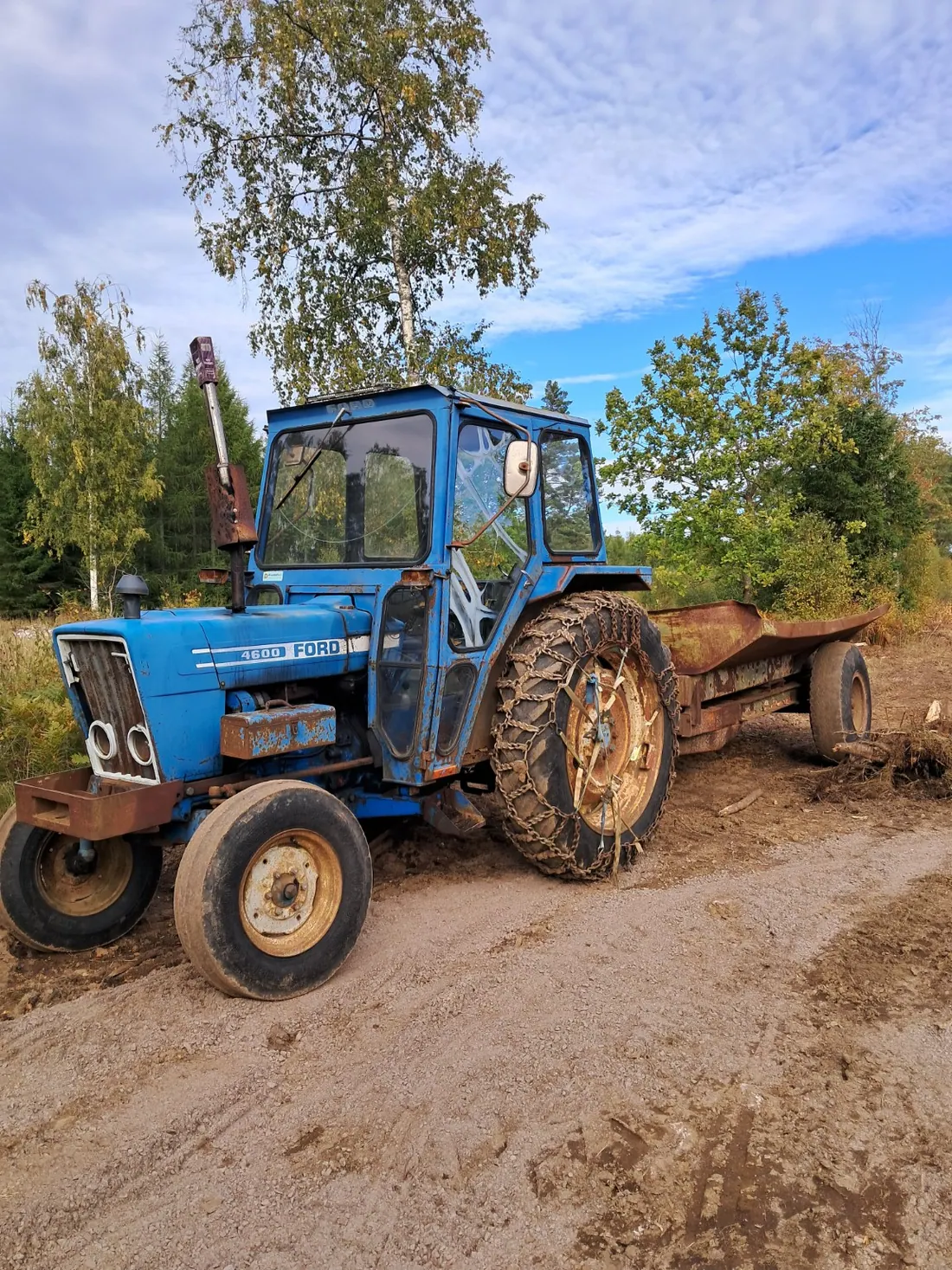 Äldre blå Ford-traktor med vagn utomhus